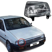 A headlight assembly for a Maruti Suzuki Zen, shown next to the corresponding side of a white Maruti Suzuki Zen car. The headlight is off-white in color, with a clear lens and reflector.